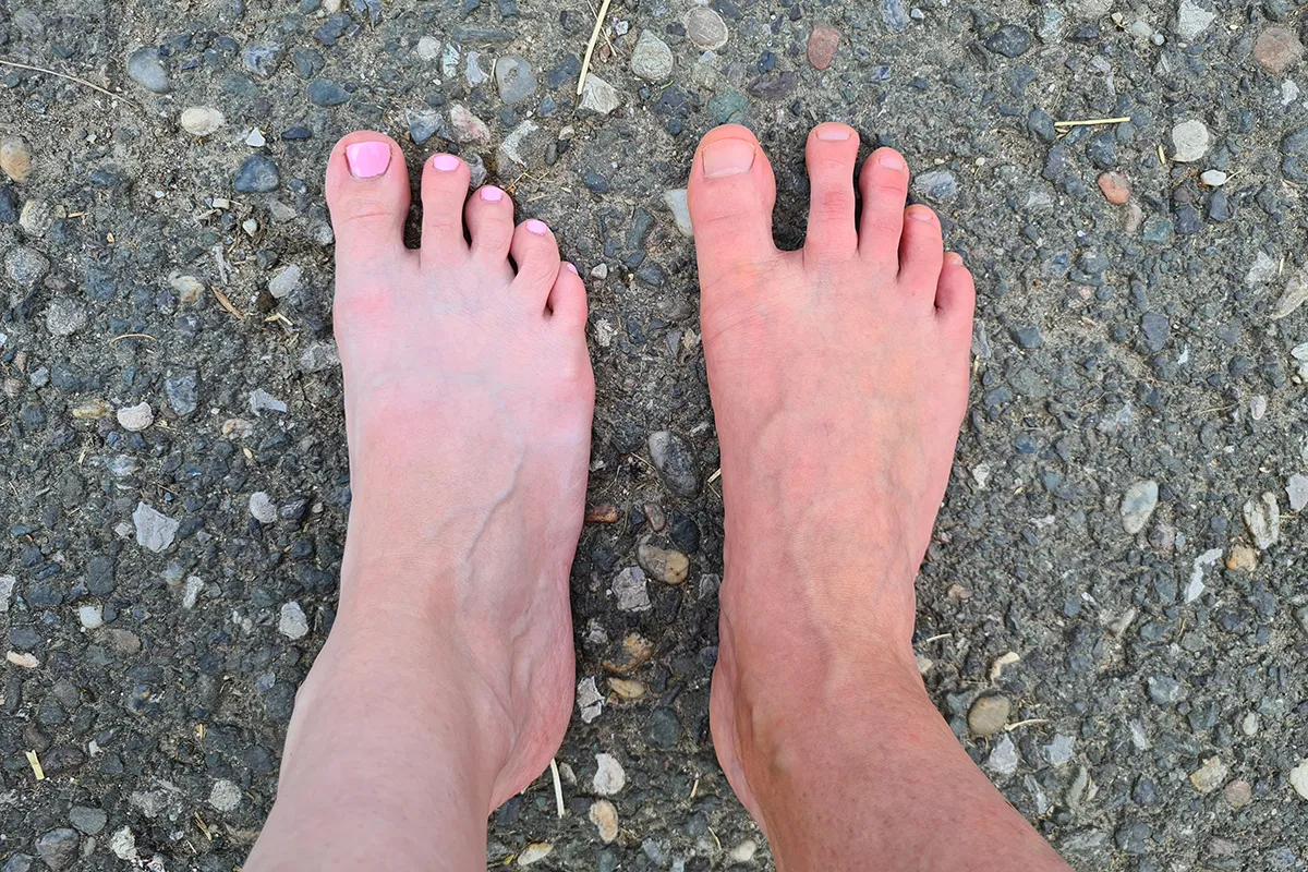 Two bare feet on a gravel surface showing natural toe splay and different foot shapes.