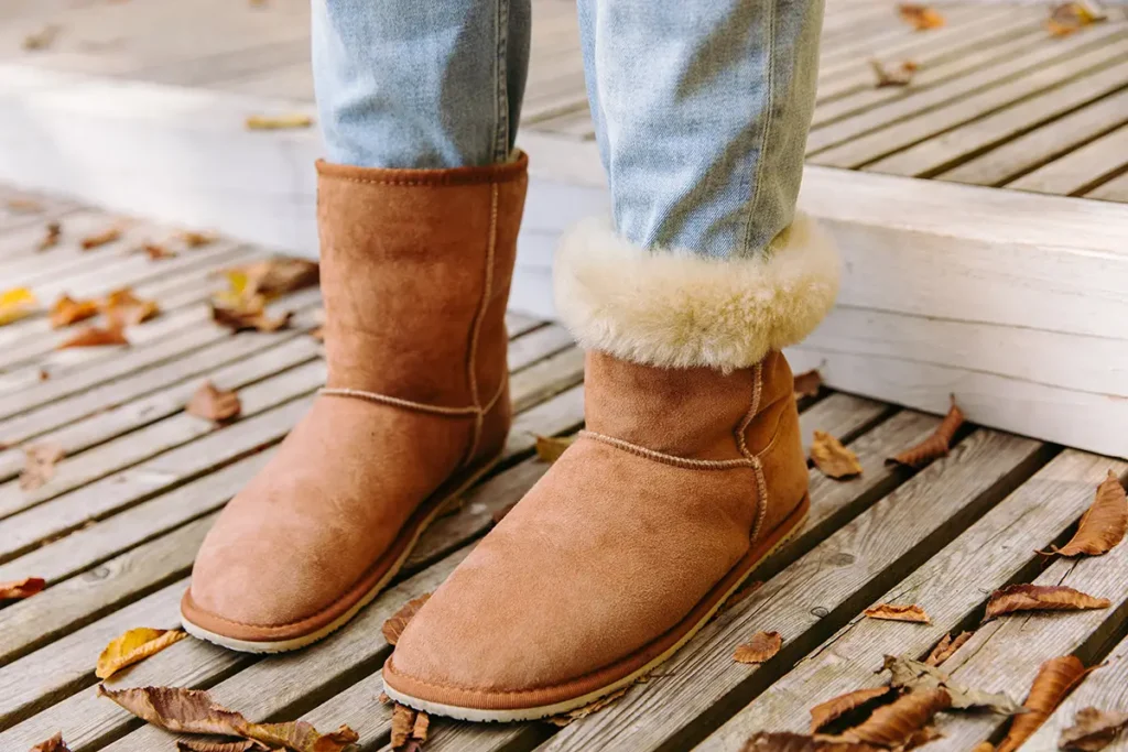 Brown suede barefoot winter boots with shearling lining worn outdoors on a wooden deck.