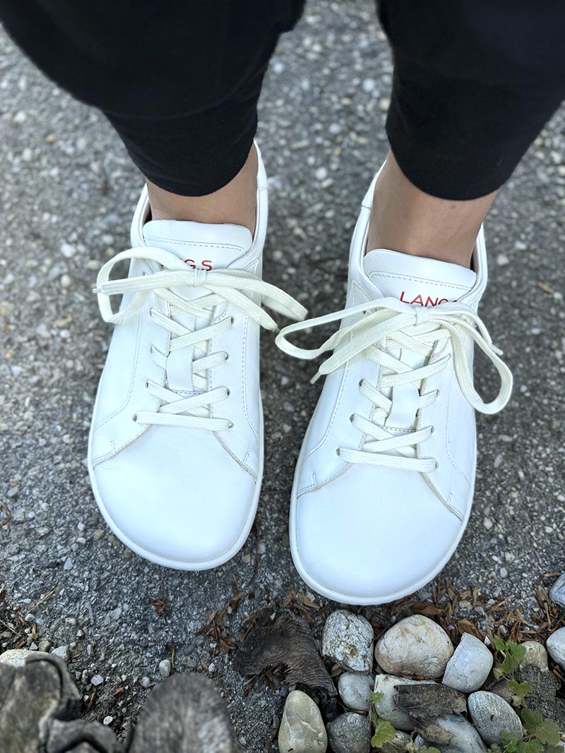 White low-top sneakers worn outside on stone pavement, top-down view