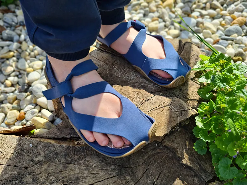 Blue kids barefoot sandals worn outdoors on a tree stump