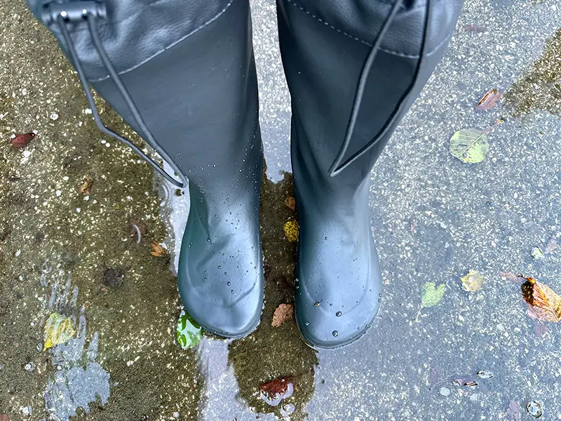 Black waterproof barefoot rain boots standing in a shallow puddle.
