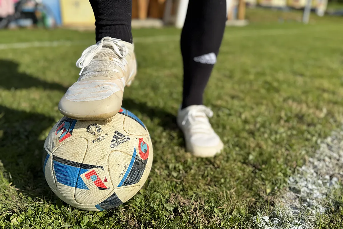 White barefoot soccer cleats stepping on the ball near the sideline.