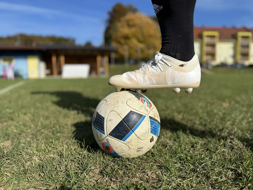 White barefoot football cleats resting on top of a soccer ball on the field.