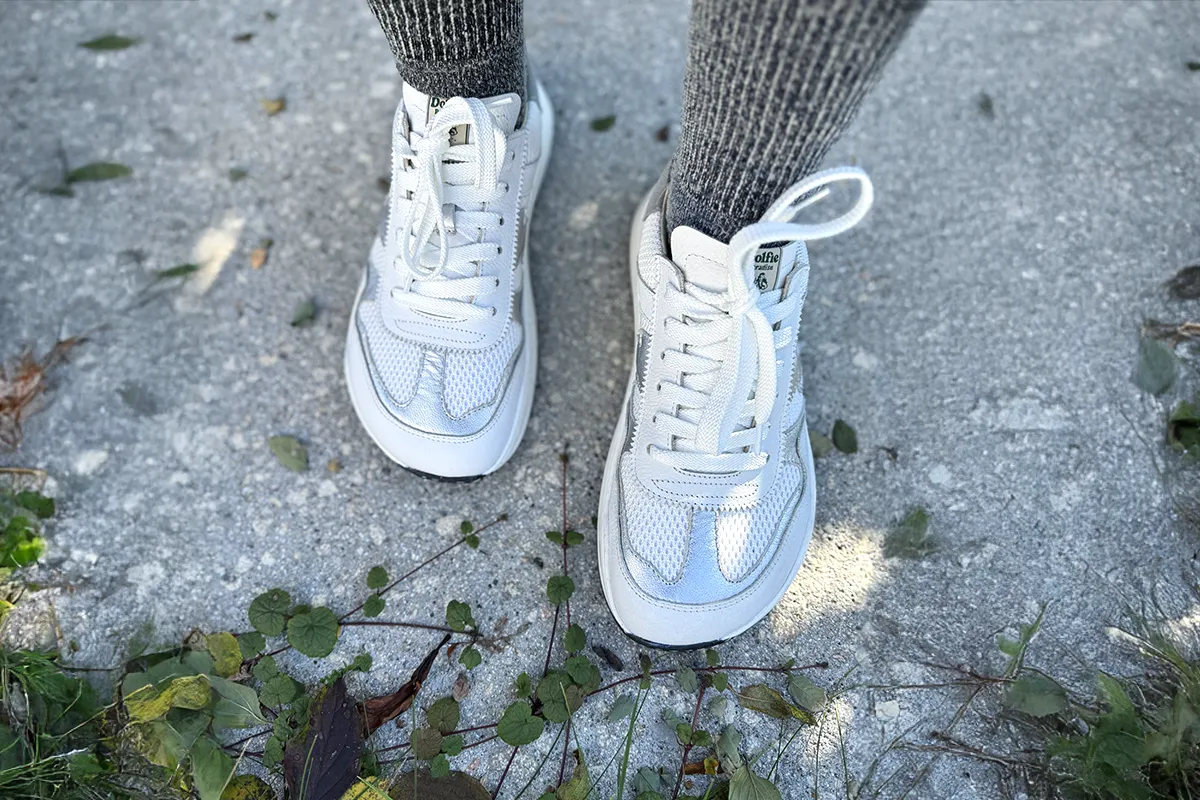 White sneakers worn outdoors on pavement, viewed from above