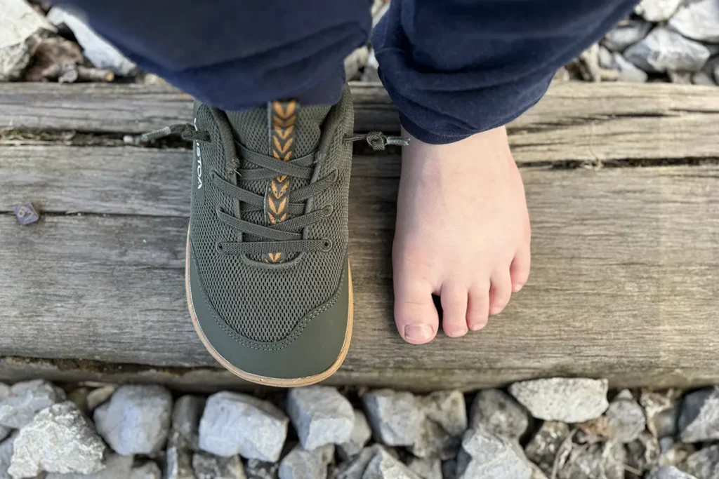 Green kids barefoot sneakers next to a bare foot