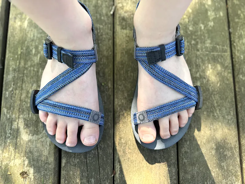 Blue barefoot sandals with ankle straps worn outdoors